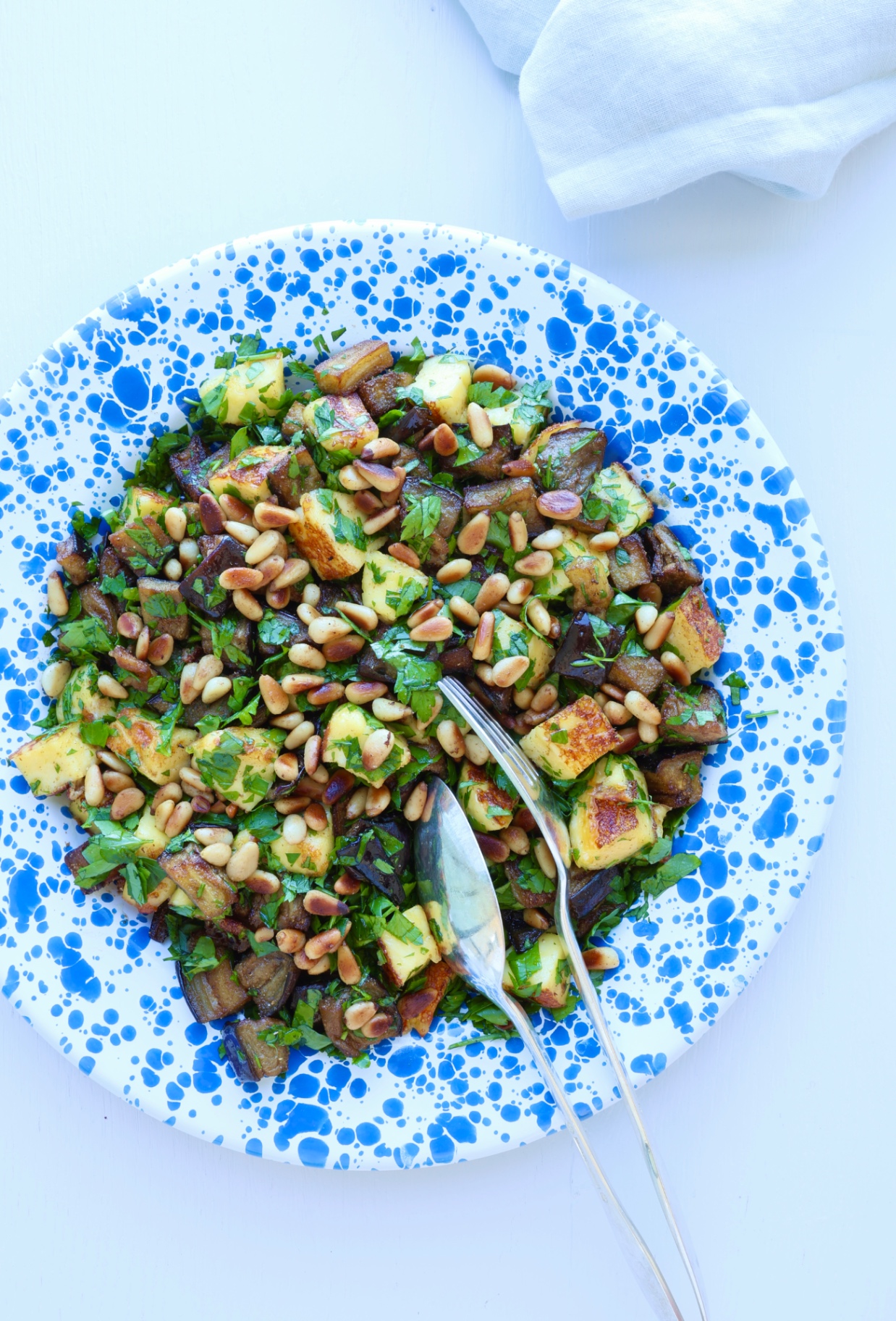 Roasted eggplant with grilled cheese, fresh herbs and toasted pine nuts on a blue splatter plate