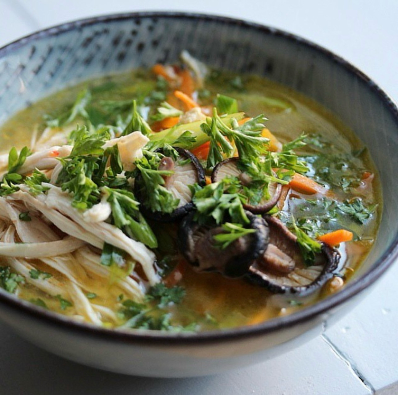 Bowl of clear chicken broth with shredded chicken, shiitake and parsley